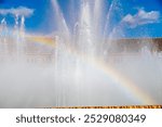 Sevilla, Sevilla - Spain – 04-19-2024: Sunlight creates a rainbow within the water spray of Plaza de España’s grand fountain, set against a clear sky.