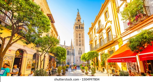 SEVILLA, SPAIN - 15 March, 2019: City view with Seville Cathedral and Giralda tower. Summer cafes on Calle Mateos Gago street.