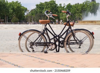 Seville, Andalusia, Spain; April 26th 2022: Vintage Style Bicycles Tied Up In The Plaza De España. Two Bicycles Together Leaning Against A Kerb In A Pedestrian Square.