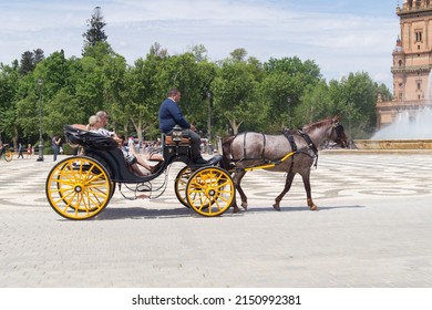 Seville, Andalusia, Spain; April 26th 2022: Older Couple Riding Around The Plaza De España In A Horse-drawn Carriage. Tourist Couple Sitting In A Carriage In A Tourist Area Of The City On A Sunny Day.