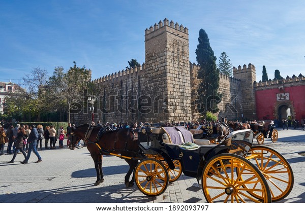 Seville, Andalusia, Spain, Europe.\
01-02-2017, Horse carriage and view of the Lion\'s Gate in the Real\
Alcazar of Seville and row of people waiting to\
enter