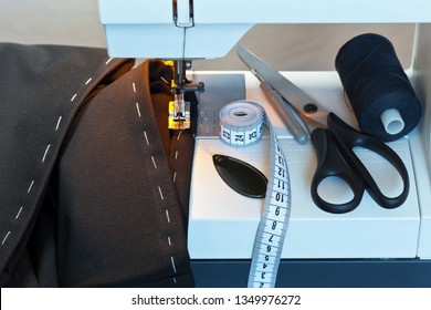 Sew At Home. Processing The Bottom Of The  Trousers On The Sewing Machine. Sewing Accessories: Black Thread, Needle Threader, Scissors And Measuring Tape