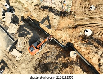 Sewage Drainage System Mounting At Construction Site. Excavator During Laying Sewer Pipe And Main Systems. Civil Infrastructure, Water Lines, Sanitary Sewers And Storm Sewers. Laying Sewer Pipes.