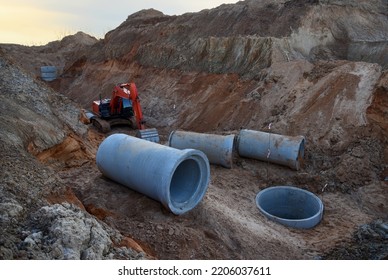 Sewage Drainage System Mounting At Construction Site. Excavator During Laying Sewer Pipe And Main Systems. Civil Infrastructure, Water Lines, Sanitary Sewers And Storm Sewers. Laying Sewer Pipes.