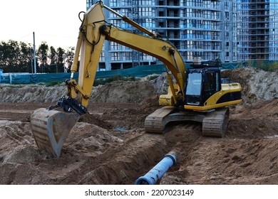 Sewage Drainage System Mounting At Construction Site. Excavator During Laying Sewer Pipe And Main Systems. Civil Infrastructure, Water Lines, Sanitary Sewers And Storm Sewers. Laying Sewer Pipes.