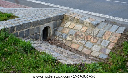 Sewer bridge through a ditch by the road. concrete hole with surroundings of stone paving. grassy slope by the road. has the task of releasing water under a turnoff by crossing roads