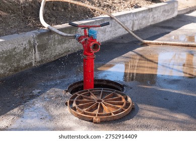 Sewer cleaning process with hydrant and hose in open manhole on city street, municipal drainage maintenance