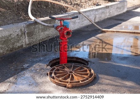 Sewer cleaning process with hydrant and hose in open manhole on city street, municipal drainage maintenance