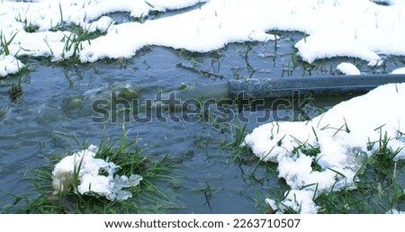 The sewer pipe drains toxic water directly to the ground. Soil contamination with water after domestic use. Dirty water flows from a pipe onto white snow.