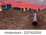 Sewer pipes laying. Sanitary drainage, external sewage. Tower crane on building construction. Excavator dig trench on construction site. Stormwater dig and pipe underground. Water infrastructure.