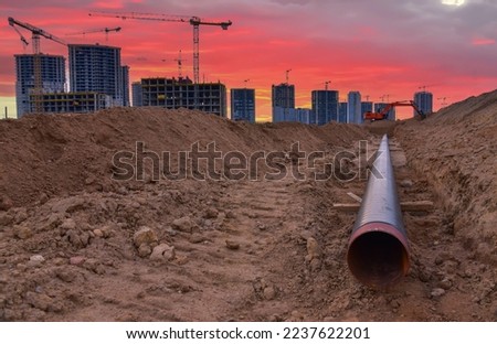 Sewer pipes laying. Sanitary drainage, external sewage. Tower crane on building construction. Excavator dig trench on construction site. Stormwater dig and pipe underground. Water infrastructure.