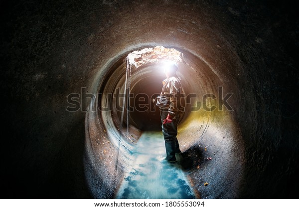 Sewer tunnel worker examines sewer system damage\
and wastewater leakage.