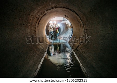Sewer tunnel workers examines sewer system damage and wastewater leakage