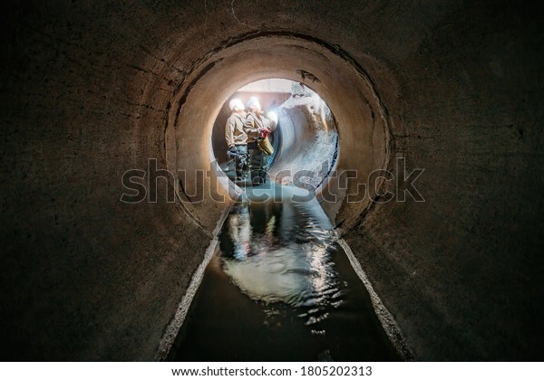 Sewer tunnel workers examines sewer system damage\
and wastewater leakage