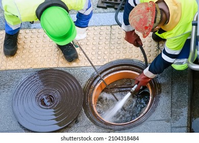 sewer  utility worker for cleaning and repairing sewerage pipes  in city street - Shutterstock ID 2104318484