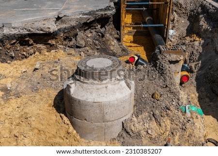 A sewer well excavated for repair with a metal manhole and new pipes connected to it.