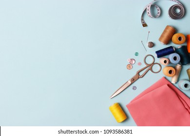 Sewing Accessories And Fabric On A Blue Background. Sewing Threads, Needles, Pins, Fabric, Buttons And Sewing Centimeter.
 Top View, Flatlay