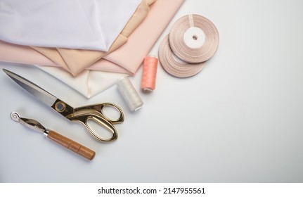 Sewing Accessories And Fabric On A White Background. Sewing Threads, Needles, Pins, Fabric, Buttons And A Sewing Centimeter. Top View, Flatlay