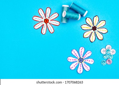 Sewing accessories on a blue background. Sewing threads in blue colors and buttons. Paper cut our flowers. Top view with room for copy. 
