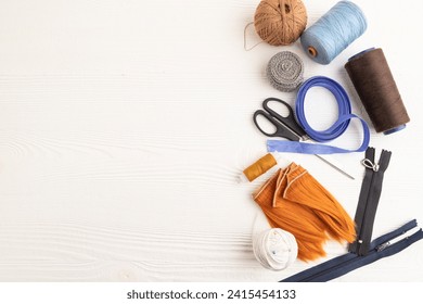 Sewing accessories: scissors, thread, thimbles, braid on white wooden background. Top view, flat lay, copy space