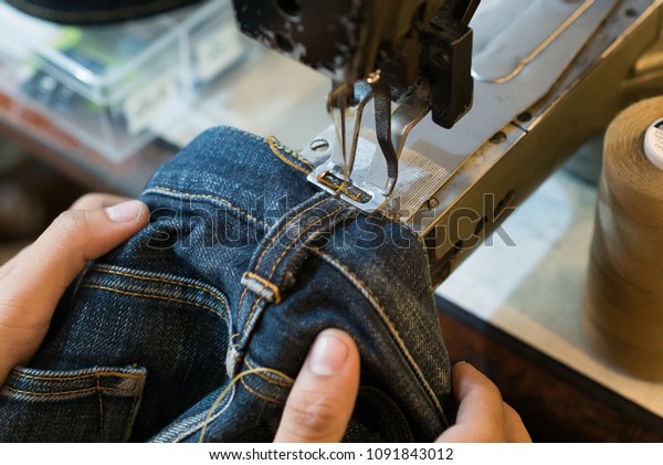 Sewing denim jeans with sewing machine. Repair\
jeans by sewing machine. Alteration jeans, handmade garment\
industrial concept.