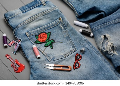 Sewing embroidered patch to a favorite pair of jeans. Trendy denim refashion, new look for worn clothes.
