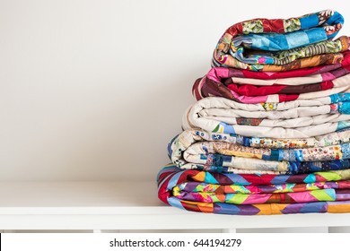 sewing and fashion concept - stack of colorful quilts, beautiful bedspreads stacked in several rows in height for storage, sale patchwork productions on a white background, copy space
