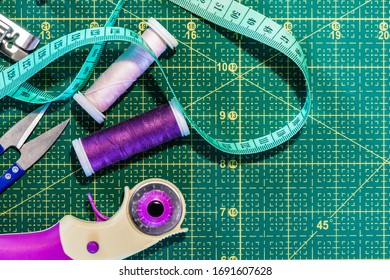 Sewing Flat Lay. Top View Of Sewing Accessories On Cutting Mat: Centimeter, Rotary Cutter, Sewing Threads And Clippers. Dressmaking Industry