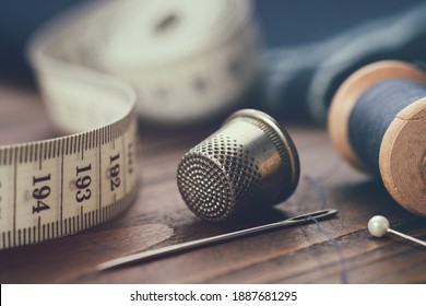 Sewing items - thimble, needle, measuring tape, spools of blue thread, including pins. Blue fabric for sewing on background. - Shutterstock ID 1887681295