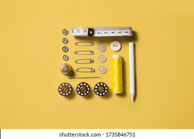 Sewing kit accessories and tools for needle work in yellow. Tape measure, pins, scissors, buttons, prewound bobbins, thimble, thread cutter flat lay. Knolling same color concept.