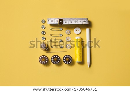Sewing kit accessories and tools for needle work in yellow. Tape measure, pins, scissors, buttons, prewound bobbins, thimble, thread cutter flat lay. Knolling same color concept.