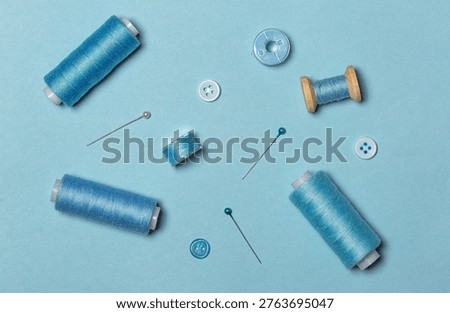 Sewing kit, blue threads on spools and sewing bobbins, buttons, top view.