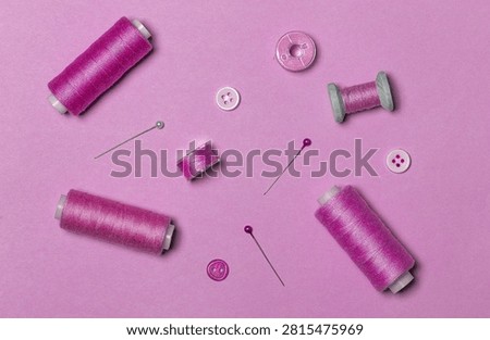 Sewing kit, pink thread on spools and bobbins, buttons, top view.