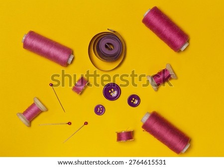 Sewing kit, red threads on spools and bobbins, buttons, top view on yellow background.