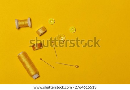 Sewing kit, yellow threads on spools and bobbins, buttons, top view.