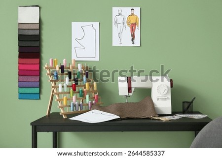 Sewing machine with cloth and thread spools on tailor's table near green wall in atelier