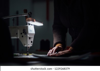 Sewing machine in dark with working hands on backdrop