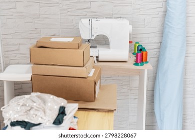 Sewing machine, fabric, thread spools, and stacked cardboard shipping boxes in a small business workshop