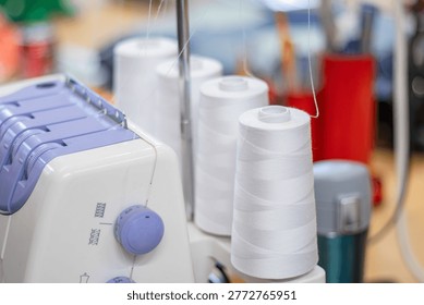 Sewing machine features multiple spools of white thread on a worktable, with various colorful sewing supplies and tools in the background