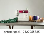 Sewing machine, green fabric and craft accessories on wooden table against light background