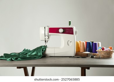 Sewing machine, green fabric and craft accessories on wooden table against light background