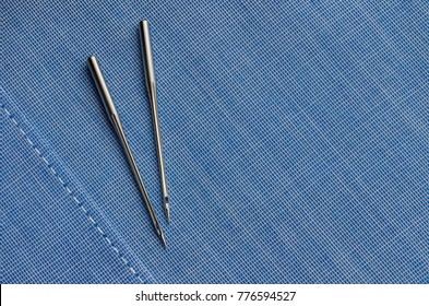 Sewing Machine Needles For Fabric Laying On Blue Cotton Cloth With A Straight White Thread Stitch