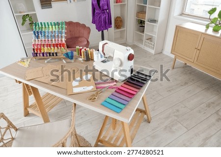 Sewing machine with patterns and thread spools on tailor's table in atelier interior