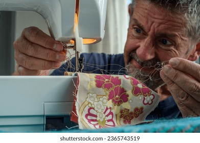 Sewing machine problems, senior man struggles and becomes frustrated when the machine goes wrong. His face say's it all. Copy space. - Powered by Shutterstock