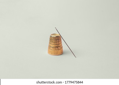 A sewing needle and a antique gold thimble. Geometric composition on a colored background.