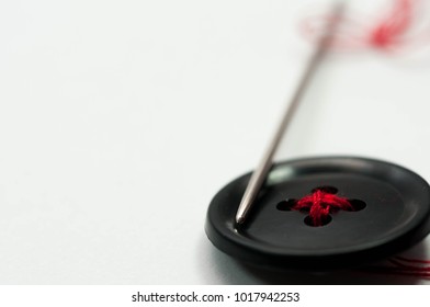 Sewing needle with red thread, black button close up macro shot isolated on white background.