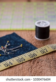 Sewing Notions Such As Fabric, Pins, Tape Measurer, Spool Of Thread And Quilting Grid Sit On Top Of A Rustic Wood Surface