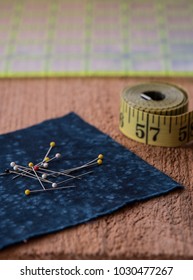 Sewing Notions Such As Fabric, Pins, Tape Measurer And Quilting Grid Sit On Top Of A Rustic Wood Surface