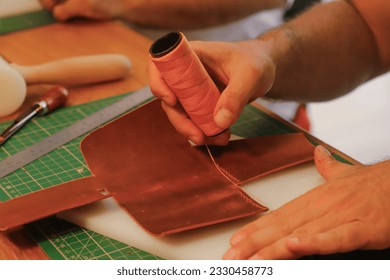 Sewing orange thread while making leather wallet in workshop.