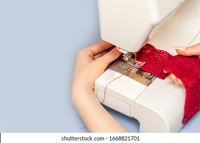 Sewing process on sewing manufacturing machine detailed by woman's hands holding red lace fabric for lingerie production. Copy space. Close up.